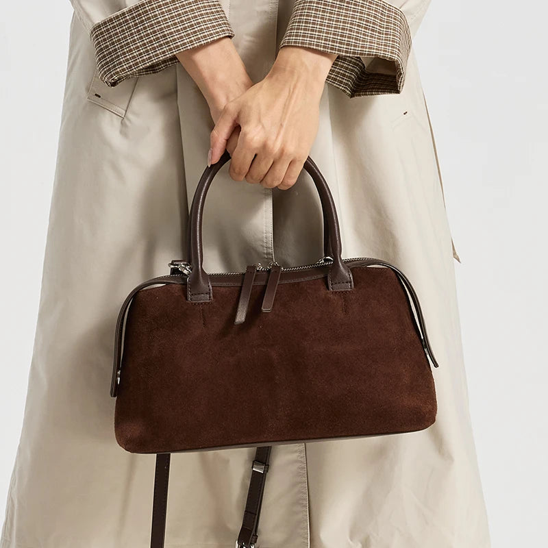 Sac marron daim foncé tenu à la main devant un trench beige