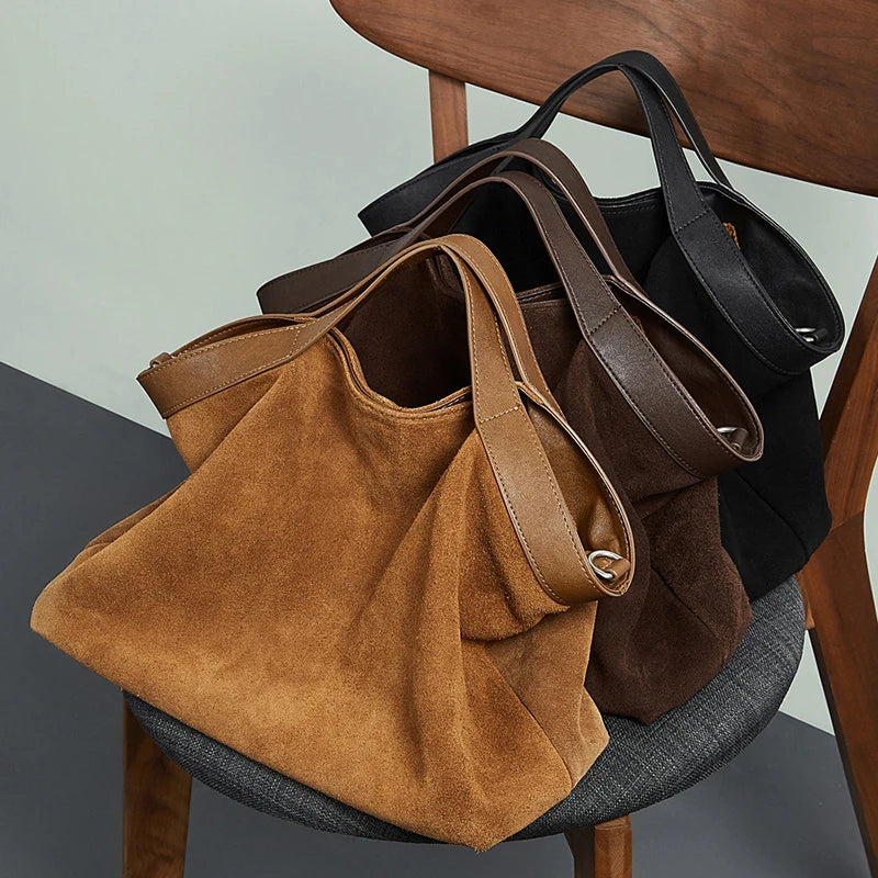 Grands sacs en daim cognac, café et noir posés sur une chaise
