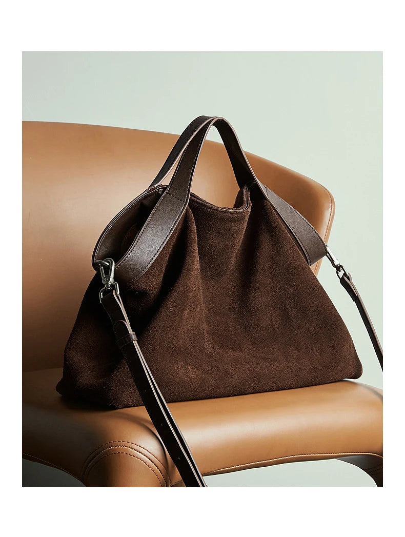 Grand sac en daim café posé sur une chaise en cuir avec sa bandoulière