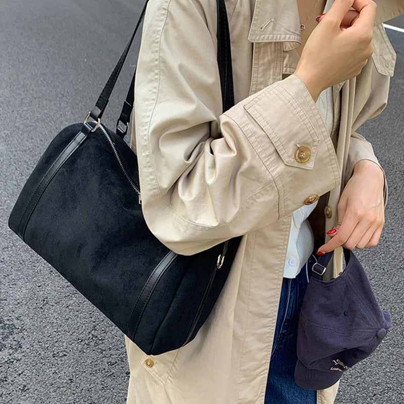 Sac polochon noir porté à l’épaule avec un trench beige