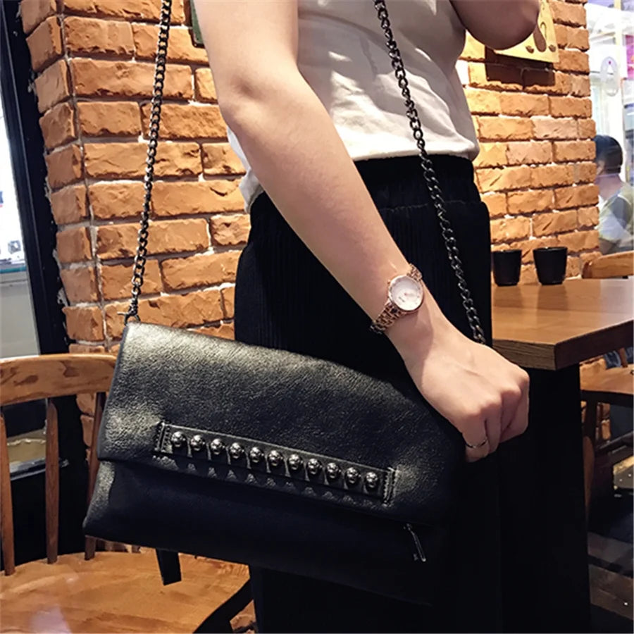 Pochette noire à rivets portée en bandoulière avec sa chaîne