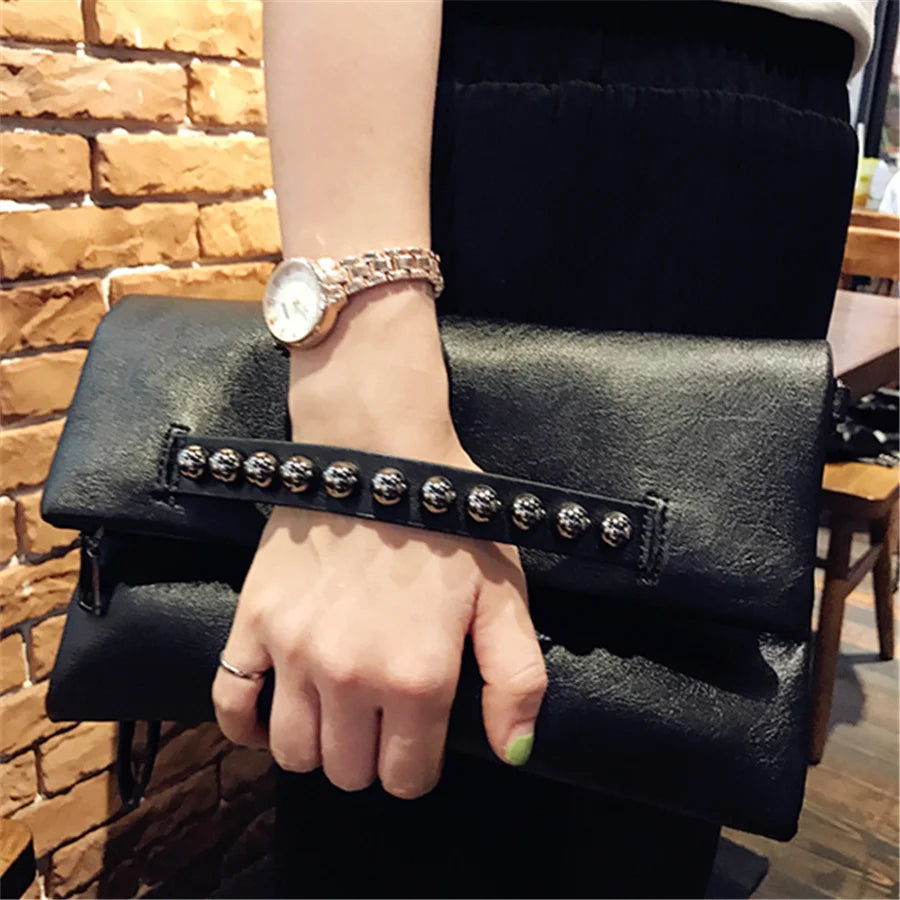 Pochette noire à rivets tenue à la main par sa bande