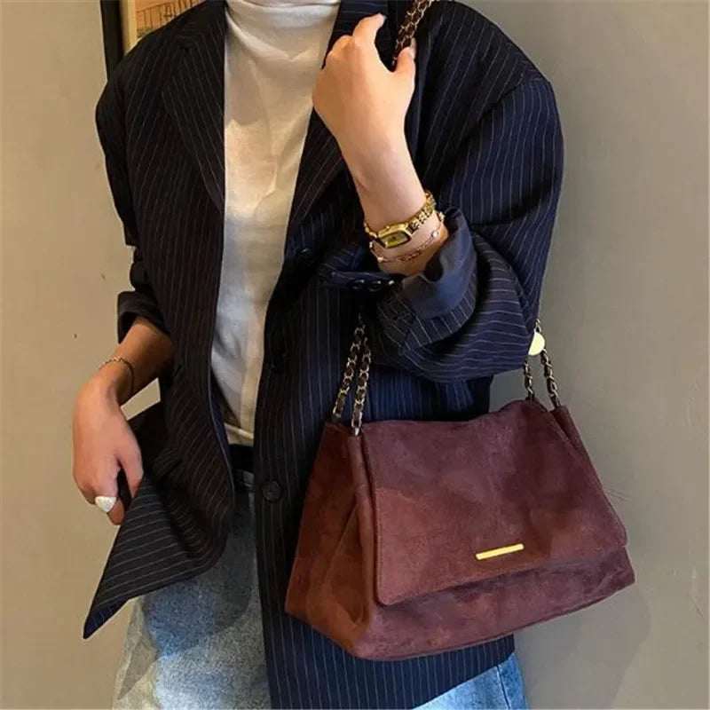 Sac bandoulière en suédine marron porté à l’épaule avec un blazer rayé