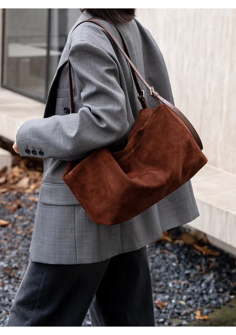 Sac en daim marron foncé porté avec un blazer gris
